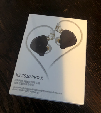 A boxed pair of KZ-ZS10 PRO X in-ear monitors. The picture shows 2 black headphones, with braided grey cables.