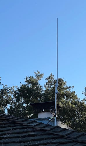 A stick-like radio antennas attached to a short mast on the roof of a house, against a clear blue California sky