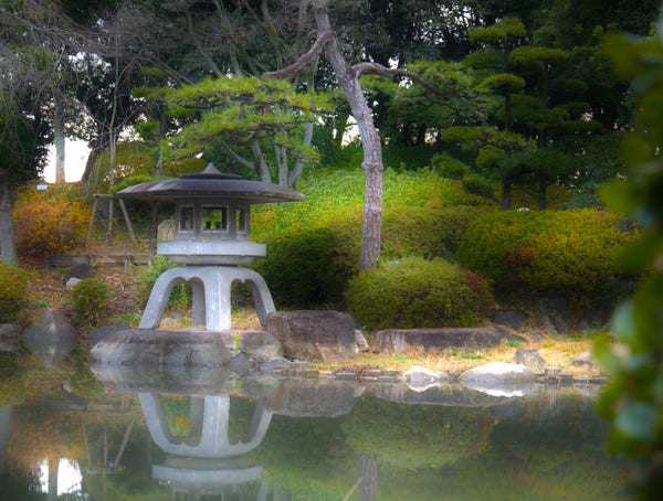 A stone lantern reflected on a calm pond surrounded by lush greenery in a tranquil garden setting in Osaka-jo.