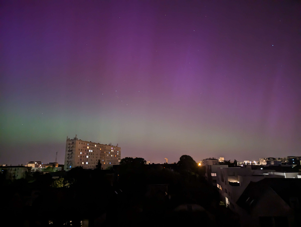 night photograph from a building of the city skyline showing the aurora borealis in the sky, with a green arc below purple strains