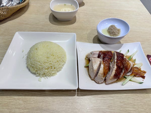 A plate of Hainanese chicken rice with sliced chicken, cucumber, rice, and condiments.
