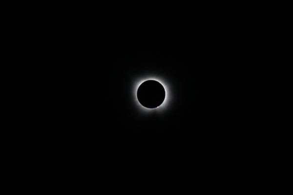 Total eclipse with a ring of light and corona around a dark sun. A flare is visible at the bottom of the sun