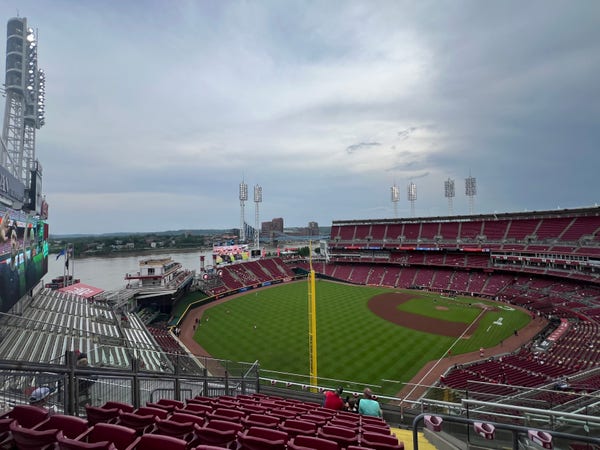 A baseball stadium with a view of the field and surrounding seating areas, including a large scoreboard on the left, under an overcast sky. The Ohio River and buildings are visible in the background.