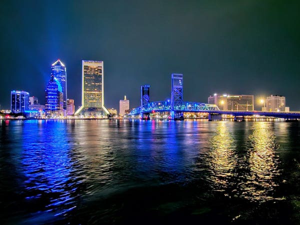 Late night view across the Saint Johns River from county boat ramp on the southbank. The Main Street (John T. Alsop Jr.) Bridge glows blue along with several office buildings along the downtown skyline, each reflecting upon the calm, dark waters below.