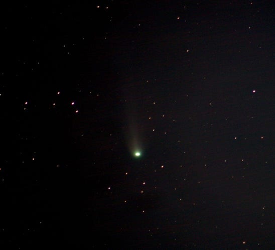Green comet Pons-Brooks at centre. A tail visible. Numerous star dots. 