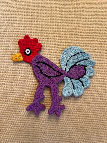 A rooster made of yarn, looking like a dense, knotted kind of flat crochet 