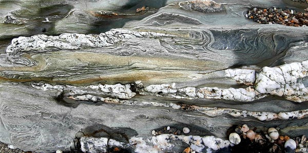 Rippled and folded rock bands with quartz deposits. Sea water is in some hollows; gravel is also present. These are the likely agents of the erosion of the bedrock.