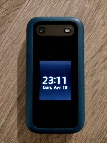 Photo du Nokia 2660 flip 4g de couleur bleue et noir. C'est un téléphone à clapet qui est fermé et un petit écran affiche l'heure et la date. Le téléphone est posé sur une table en bois.