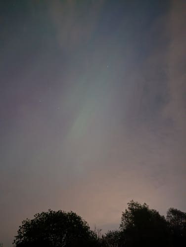 Photo nocturne d'un ciel avec une lueure verte au milieu. Il s'agit d'une aurore boréale. 