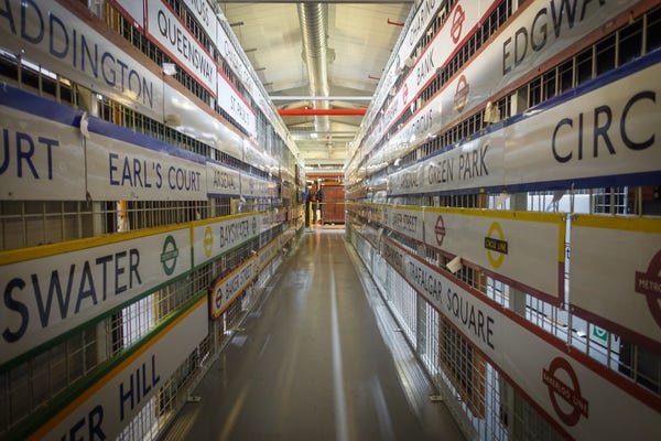 A narrow passage lined with tube station name boards of various colours. The boards are aligned and the photo is symmetrical so that they converge at a vanishing point at the far end of the passage.