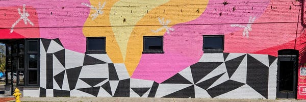 A colorfully painted business's street facing side with abstract designs in bright pink, yellow, red, and black & white checkerboard patterns.