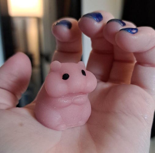 Davey's tiny hand holding a pink hamster mochi. it has a flared head and chubby body and is not intentionally phallic probably 