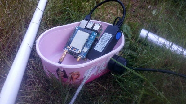 A Barbie raspberry ice cream box, with a Raspberry Pi and a PoE splitter stuffed inside. An antenna is one one side, an aluminium pole is on the other.