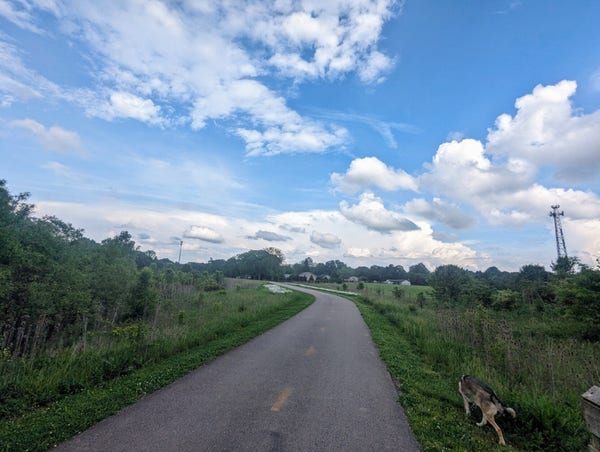 A hot cloudy day it's muggy there's rain clouds moving about for scattered showers we're on a bike path it's green the skies are peeking through blue between the clouds