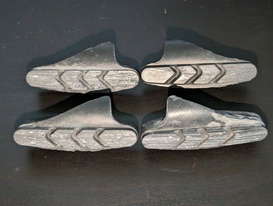 A set of 4 road bike brake pads, with embedded chunks of metal from the rim.