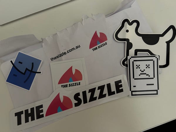A stack of stickers for The Sizzle, a finder, sad mac and Claris the dogcow