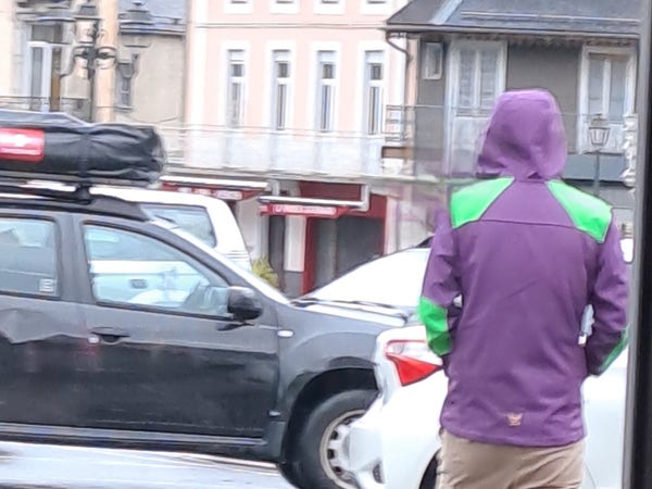 Un homme de dos sur un parking pluvieux porte un kway dont les couleurs coïncident avec celles de l'EVA-01 dans Evangelion