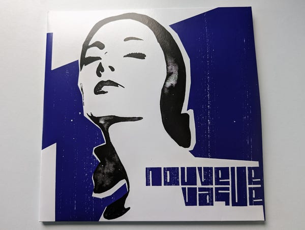 Vinyl album cover on a white surface. The album artwork is very simplistic with a rough, high contrast print of a woman's head and neck, face tilted up with eyes closed, black hair pulled back from her face and falling behind her across one shoulder. This is against a primarily blue rough print background with some white areas and the words Nouvelle Vague are written in a rough, blocky style to the bottom right.