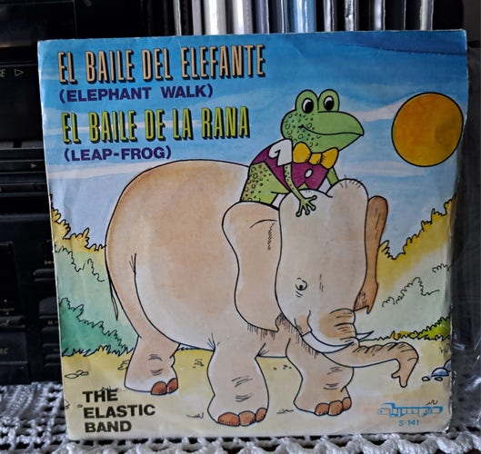 The Elastic Band:
El Baile Del Elefante (Elephant Walk)
El Baile De La Rana (Leap-Frog)

A 7" record sleeve, with the drawing of a frog 🐸 riding an elephant 🐘 under the sun 🌞