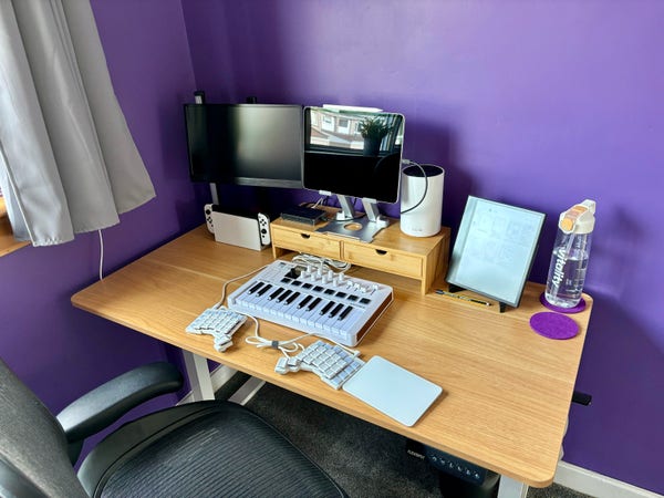 Desk with mini MIDI keyboard, split computer keyboard, and iPad on stand atop a bamboo riser with drawers.