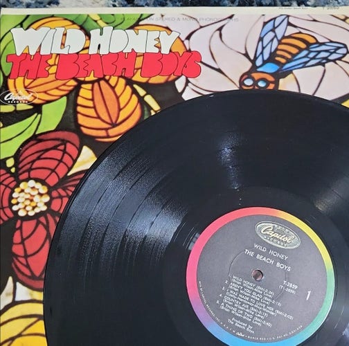 The vinyl version of the Beach Boys' 1967 album Wild Honey. The actual vinyl is sitting on top of the cover of the album and you can see the albums cover art, which is a bee and flowers from a stained glass piece that was in Brian Wilson's home. 