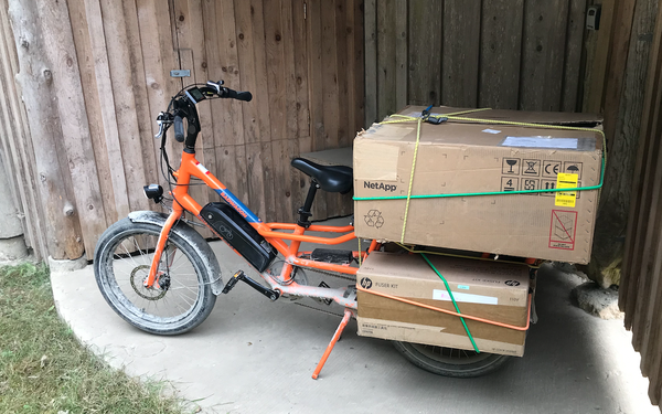 A bright orange RadPower cargo bike with a 120 pound NetApp filer on the back rack.
