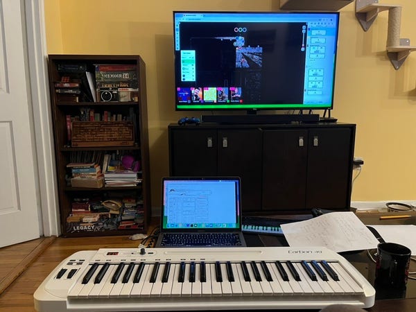A view of my living room: coffee table with a four-octave musical keyboard, an iPad, and a MacBook, facing a full-sized television set up against the far wall. The TV has a Roll 20 D&D game in progress; the laptop screen shows a D&D character sheet.