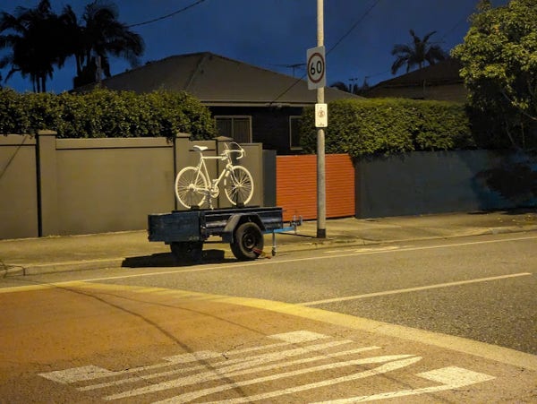 A picture of a white "ghost bike" sitting on a trailer parked on the side of the road.