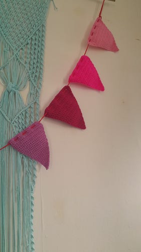 A string of crocheted bunting which is in an array of pinks, purples and pastal colours.