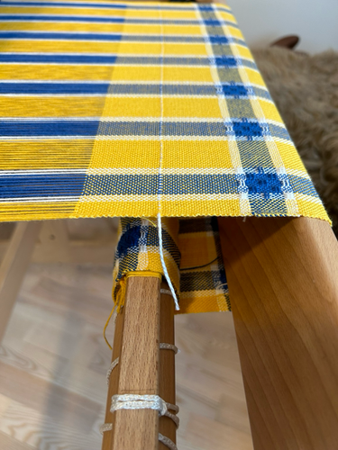 View of the cloth beam and fell of yellow and blue handwoven tea towel