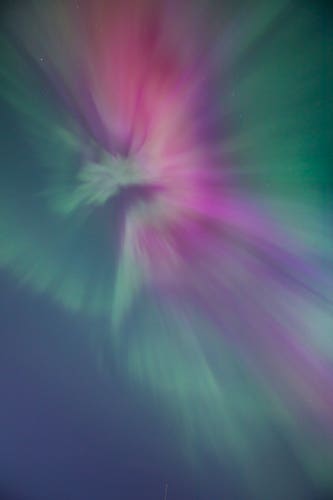 An abstract explosion of pink and teal, expanding towards the viewer - looking directly up at the aurora.