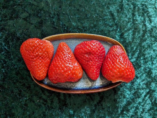 Vier Hälften von roten Erdbeeren, die in einer blauen Schale so arrangiert sind, dass sie das Logo von VIVA andeuten.