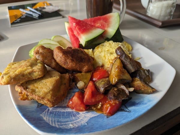 Breakfast plate of fried stuffed tofu, eggs, eggplant and tomato stewed, fried banana, and watermelon. 