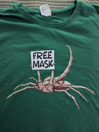 A facehugger from the Alien movie holding a sign that says Free Mask