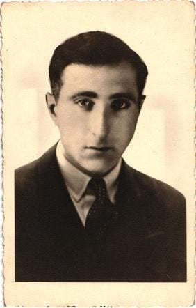 A portrait ID photo of a man in a jacket, shirt and tie. He has short dark hair and neutral expression on his face.