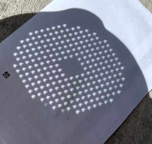 Photo of the eclipse, as seen by holding a colander over a piece of paper. The eclipse shape looks like a cookie with a bite out of it.