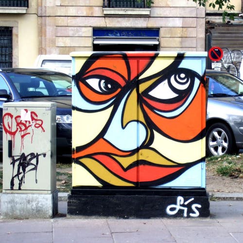 Ein Stromkasten ist mit einem Graffiti verziert, das wie ein expressionistisches, kubistisches buntes verschnörkeltes Gesicht aussieht.