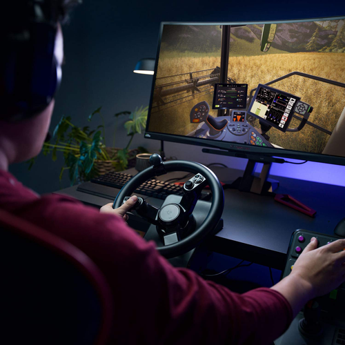 a gamer sitting at a computer desk holding a wheel peripheral. On the screen is a field of golden wheat seen from the cab of a modern combine thresher. The player's back is presumably sore from a long day's work. The smell of nacho cheese doritos hangs heavy in the air. 