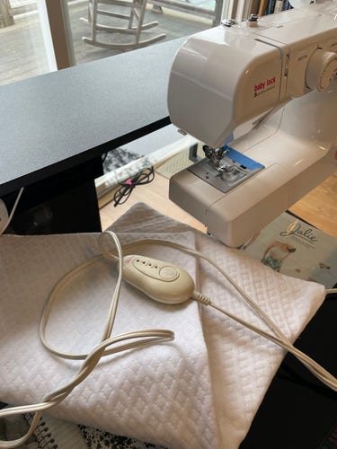 A heating pad in a white, quilted cover, next to a sewing machine.