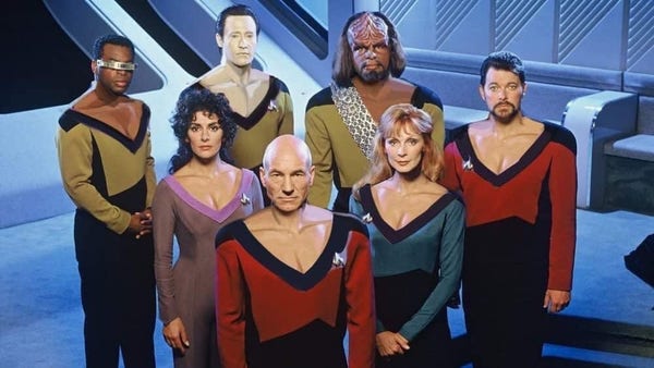 The bridge crew of the USS Enterprise (from the Next Generation) stand together facing the camera.  Captain Picard is in front, Counselor Troi and Dr. Crusher behind him, and Geordi, Data, Worf, and Riker are behind them.  All of their uniforms have been modified to have a deep V-neck like Troi's outfit.