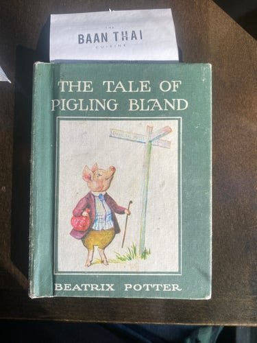 A small book with a restaurant bill sticking out the top. The book is the children’s book The tale of pigling bland by Beatrix Potter. The bill has the name of the restaurant showing, it says Baan Thai.