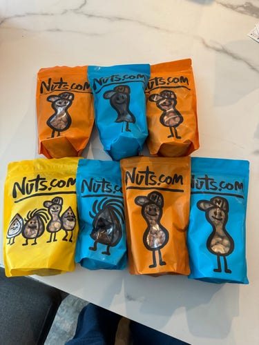 AI says “Six colorful bags with "Nuts.com" branding and cartoon nut characters. Two bags are orange, two are blue, and two are yellow. The characters on the bags have playful expressions and poses.”

I left the description as is because actually three are orange and one is yellow but you be you, AI. The rest was correct.