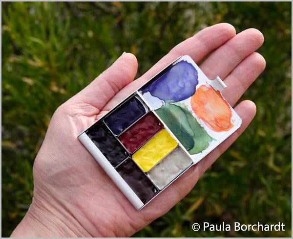 Photograph of my hand holding my new teeny tiny watercolor palette containing just 6 colors. Photo © Paula Borchardt