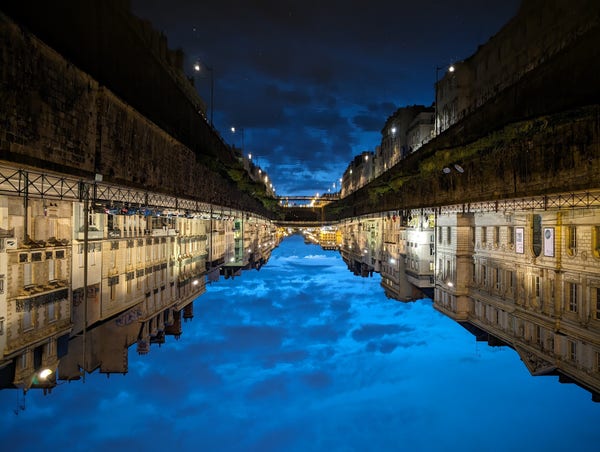 Looking over a mirrored image of a canal. The water is very smooth and the bright relfection is in stark contrast of the dark upper half.