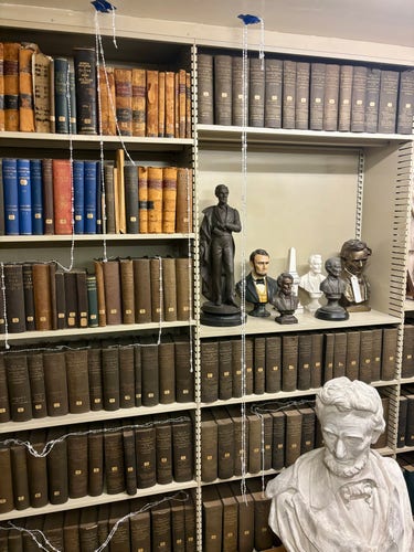 Shelves of books and some small statues. Strings of beads taped to the ceiling represent a water leak .