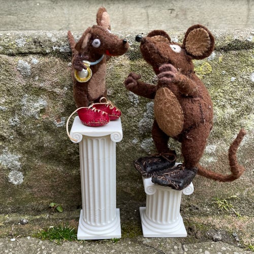 Photo of Minimus and Silvius, the Latin mice, perched on two white Ionic columns of unequal height. Silvius is on the bigger column, so he's just taller than Minimus.