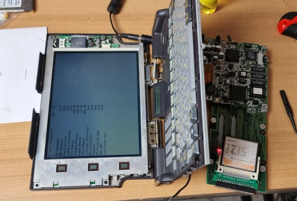 A small disassembled laptop with the bios on the screen, it's stuck on detecting the HDD 