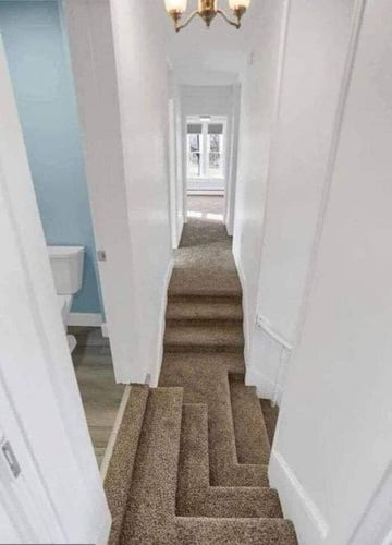A weird narrow hallway with brown carpeted stairs that go down at a right angle, with the room on the other side of the hallway with their own stairs that meet at the weird stairs. Also there's more stairs to the right.