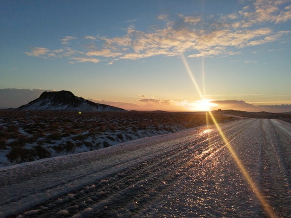 Le soleil se couche et fait briller la glace sur la route. Au fond à gauche se trouve l'Anarfell (193m alt).