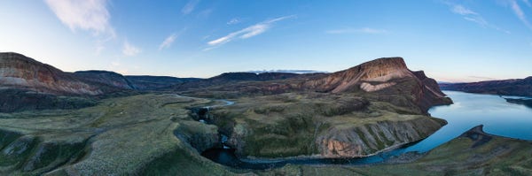 A river runs through a high valley of tundra. It then goes over two sets of falls before flowing into a calm blue fjord. Blue skies with high white clouds. 
